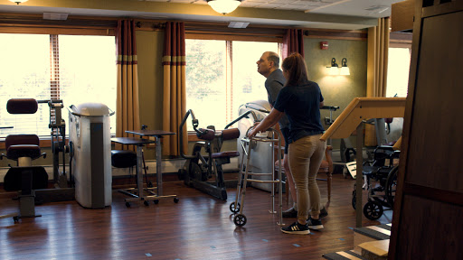 A physical therapist assisting an elderly person during a rehabilitation session in a therapy room.
