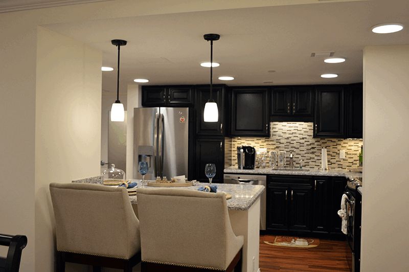 A modern kitchen with black cabinets and pendant lighting, featuring an island with seating and stainless steel appliances.