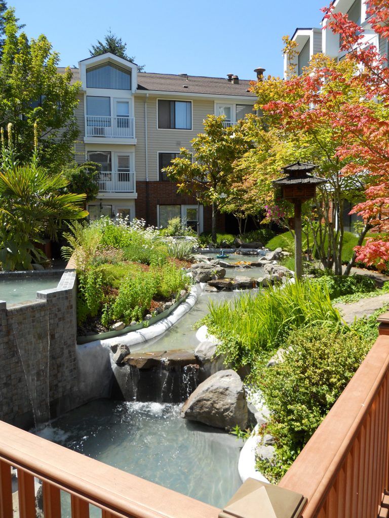 A beautifully landscaped garden with a water feature in front of an apartment building.