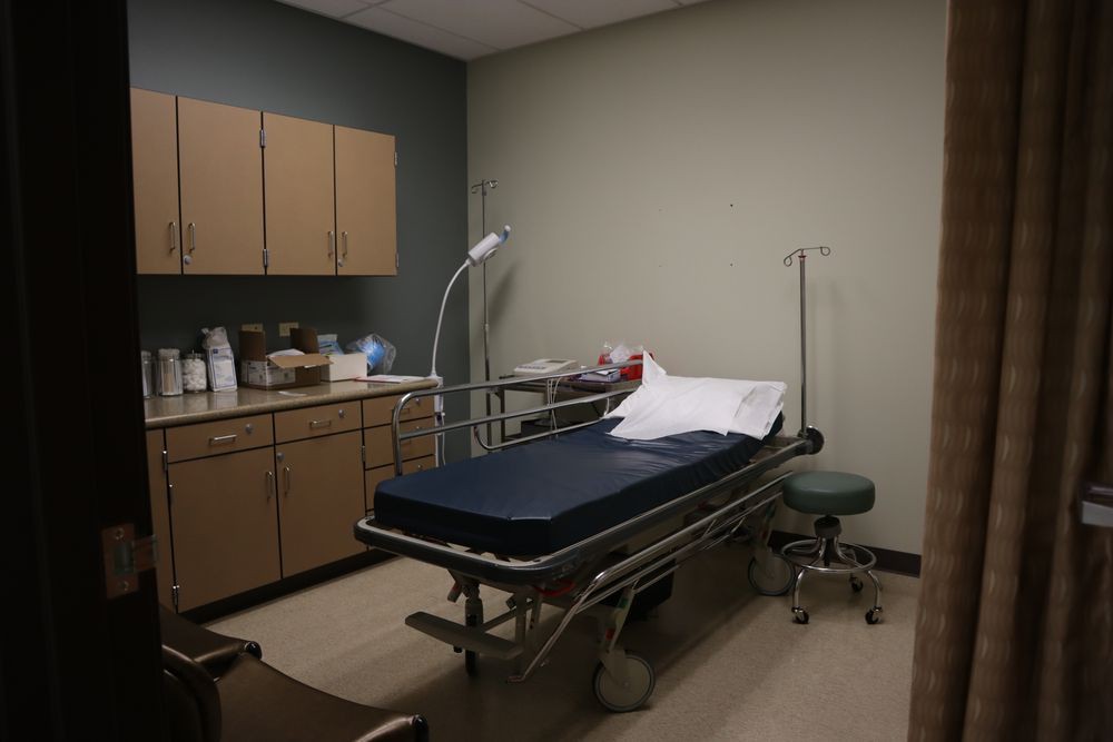 An empty hospital room with a medical bed, IV stand, and cabinets.