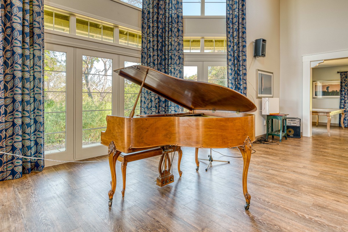 A grand piano in a spacious room with wooden floors and large windows.