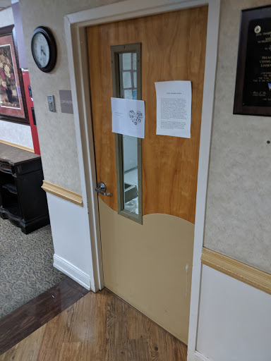 A wooden office door with a glass panel, featuring notices attached.