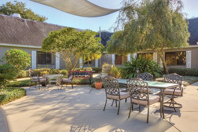 A spacious outdoor patio area featuring elegant metal furniture, surrounded by greenery and shaded by a fabric canopy.