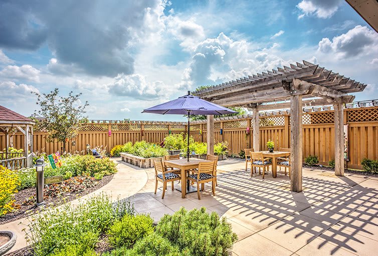 A beautifully landscaped garden patio with a pergola and outdoor seating under a blue umbrella on a sunny day.