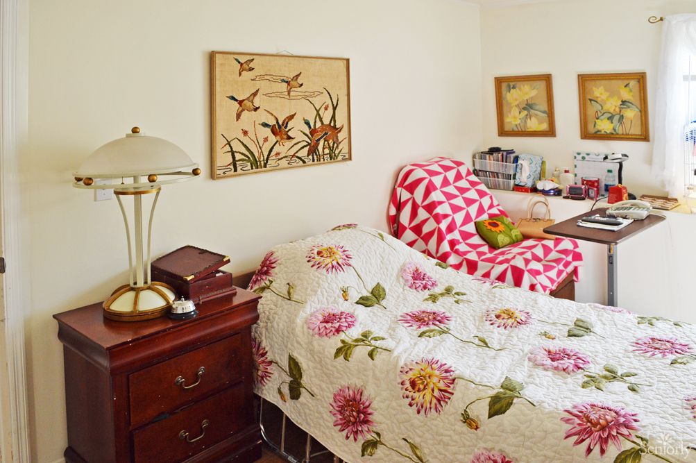A cozy bedroom featuring a floral-patterned quilt, an armchair with a geometric design, and various decorative elements.