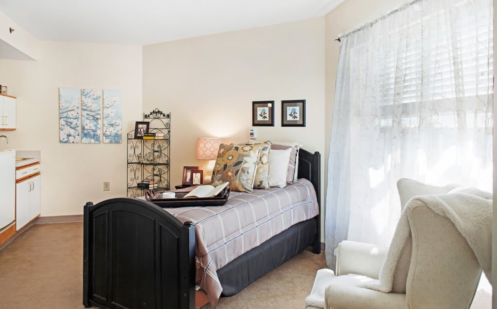 A cozy bedroom with a neatly made bed, soft lighting, and light streaming through curtains.
