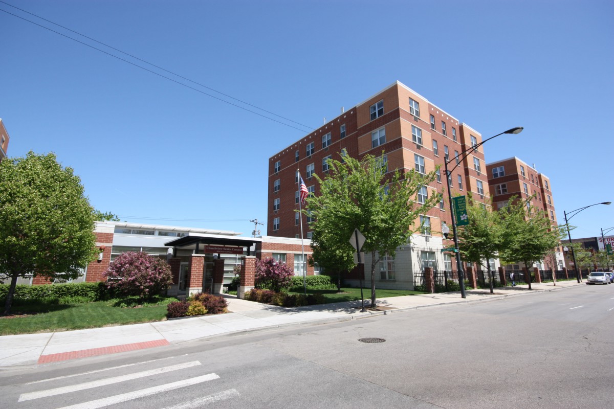A brick building in an urban setting with trees and a crosswalk.