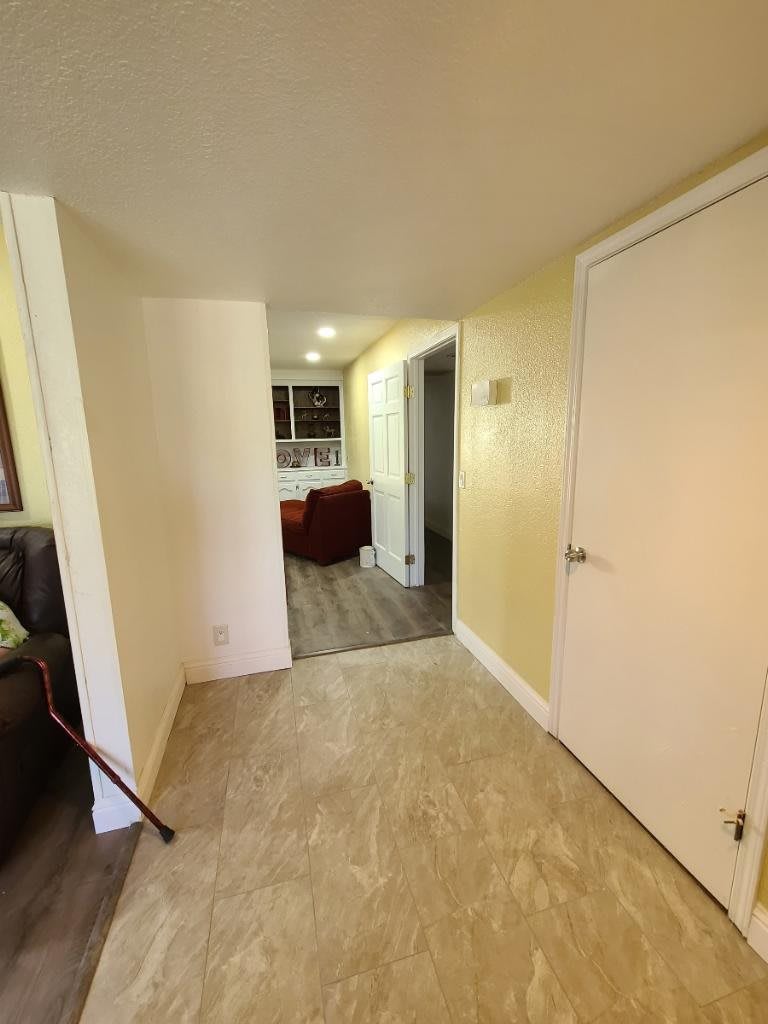 A view of a hallway leading into a kitchen area with tile and wooden flooring, and visible doors.