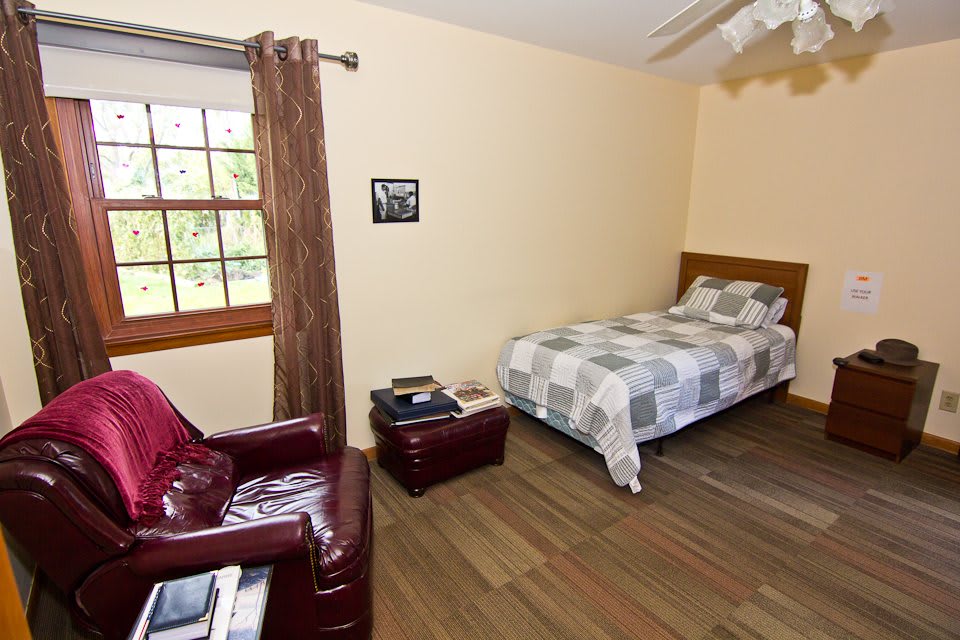 A cozy bedroom with a bed, leather chair, and a window providing natural light.