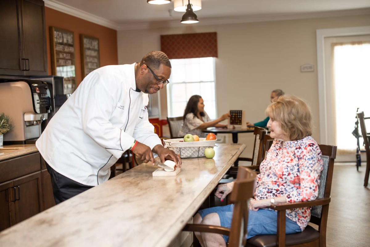 A chef serves food to a senior woman in a community setting.