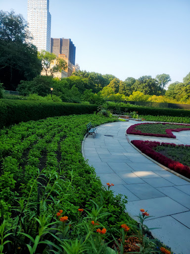 A serene garden landscape featuring well-maintained flower beds and a winding pathway amidst urban surroundings.
