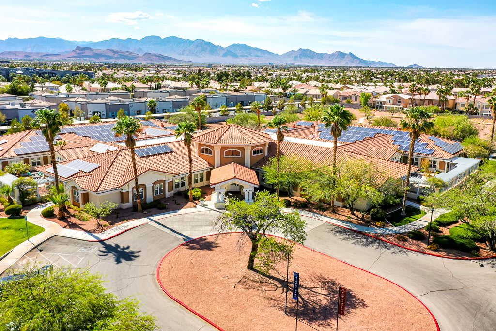 Aerial view of a suburban neighborhood with palm trees and solar panels, set against a mountain backdrop.