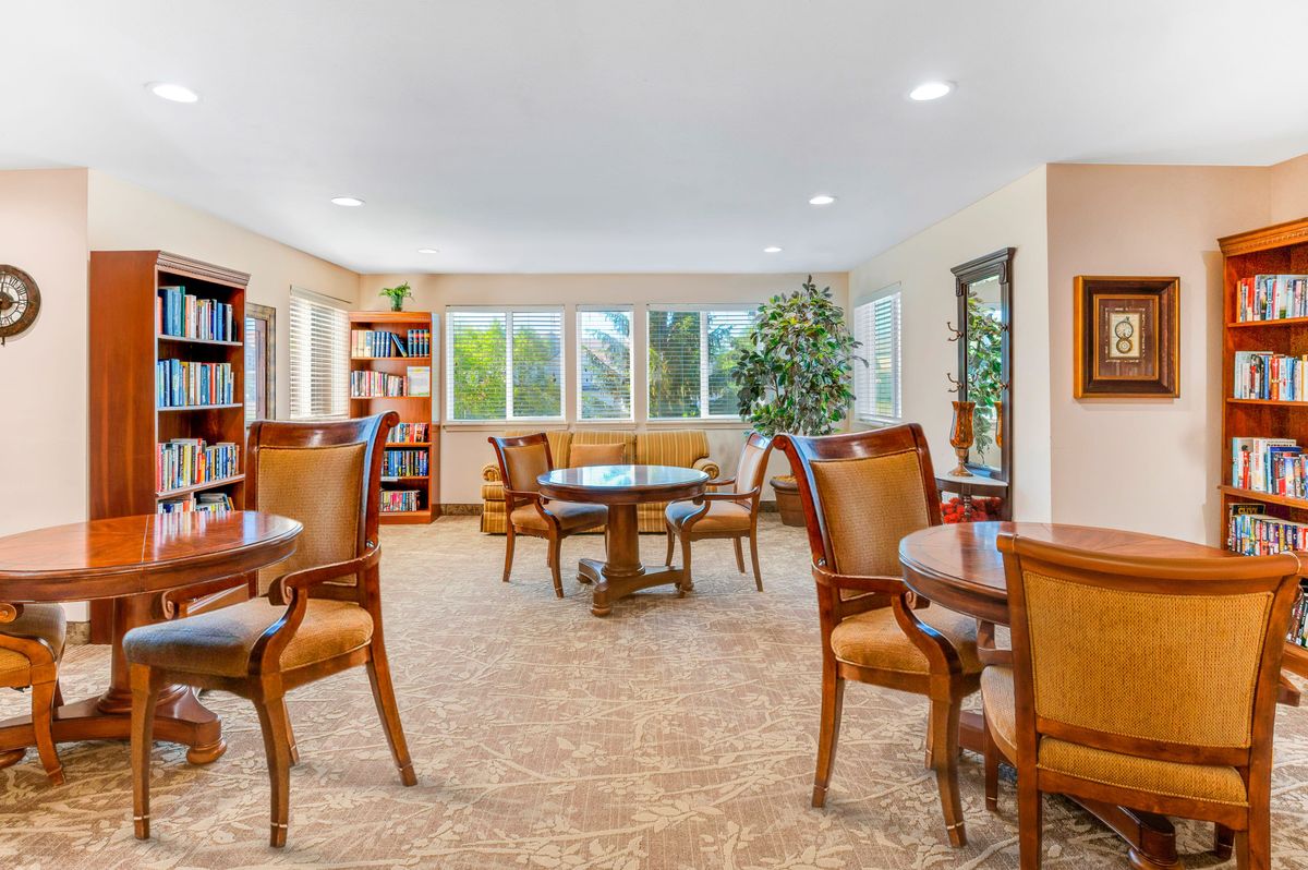 A spacious and well-lit room with multiple tables and chairs, surrounded by windows and bookshelves.