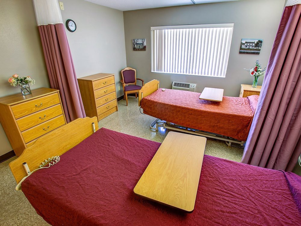 A hospital room with two beds, bedside tables, and a window providing natural light.