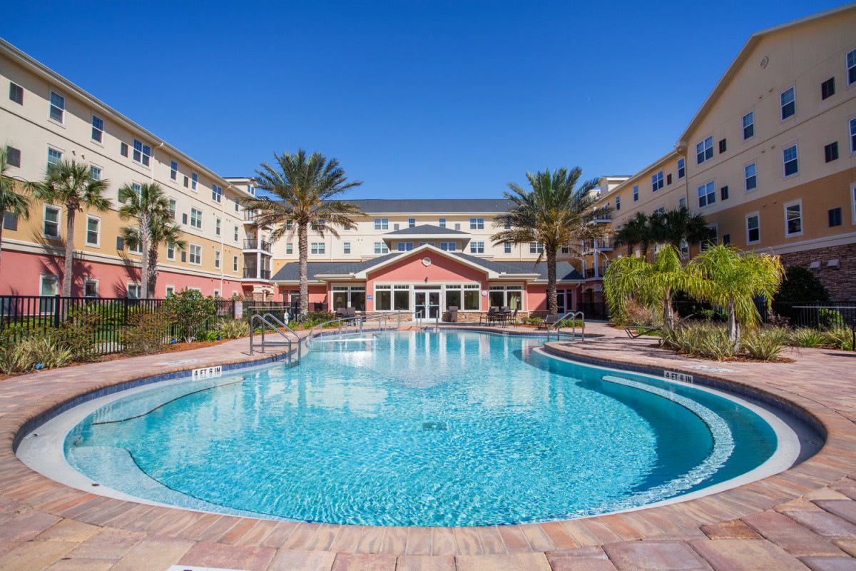 A beautiful swimming pool surrounded by palm trees at an apartment complex on a sunny day.