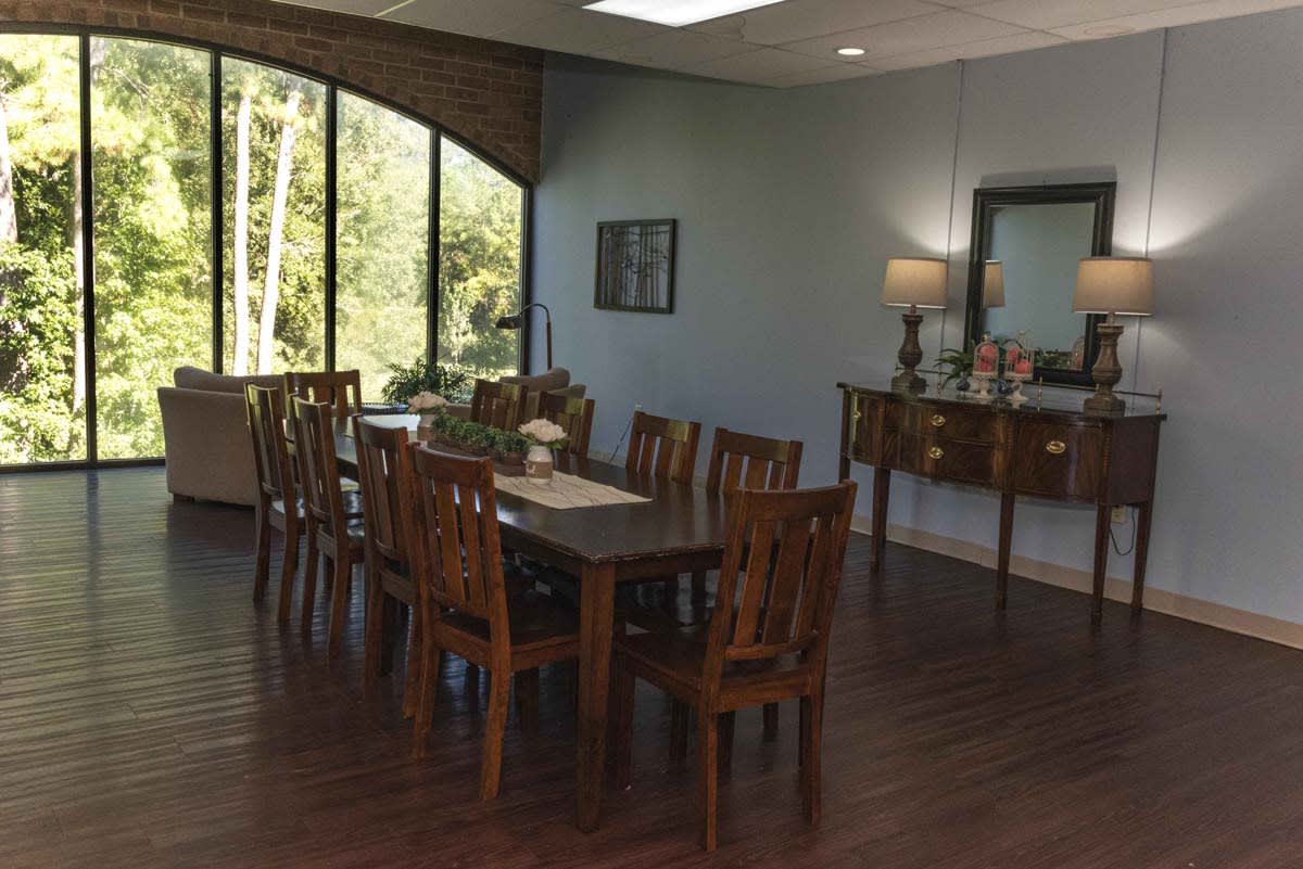 A well-lit dining room with a wooden table set and large windows offering a view of the outdoors.