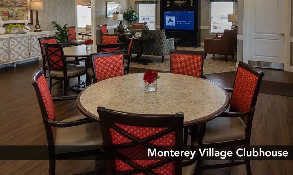 A cozy dining area with red cushioned chairs and a round table, set in a community space labeled 'Monterey Village'.