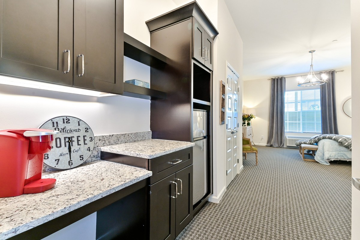 A modern kitchenette with dark cabinets and granite countertops leads into a spacious living area.