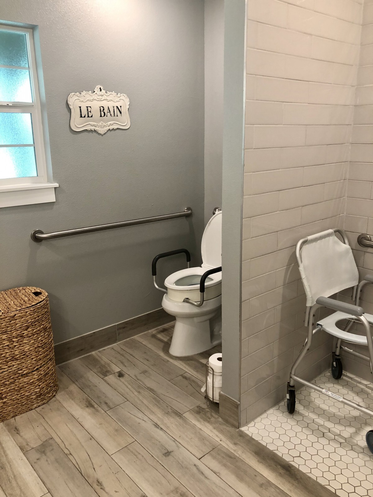 A modern, handicap-accessible bathroom with a toilet equipped with grab bars and a wheelchair nearby.