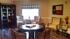 A cozy living room with a round table surrounded by chairs and a window with curtains.