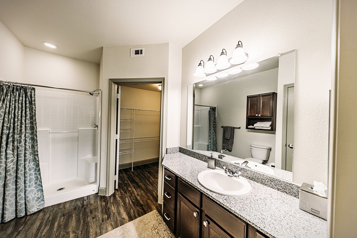 A modern bathroom with a granite-topped vanity, large mirror, and glass shower enclosure.