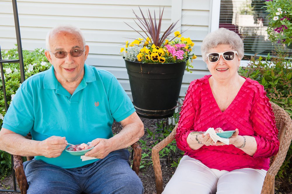 An elderly couple enjoys a sunny day outdoors, sitting together and eating.