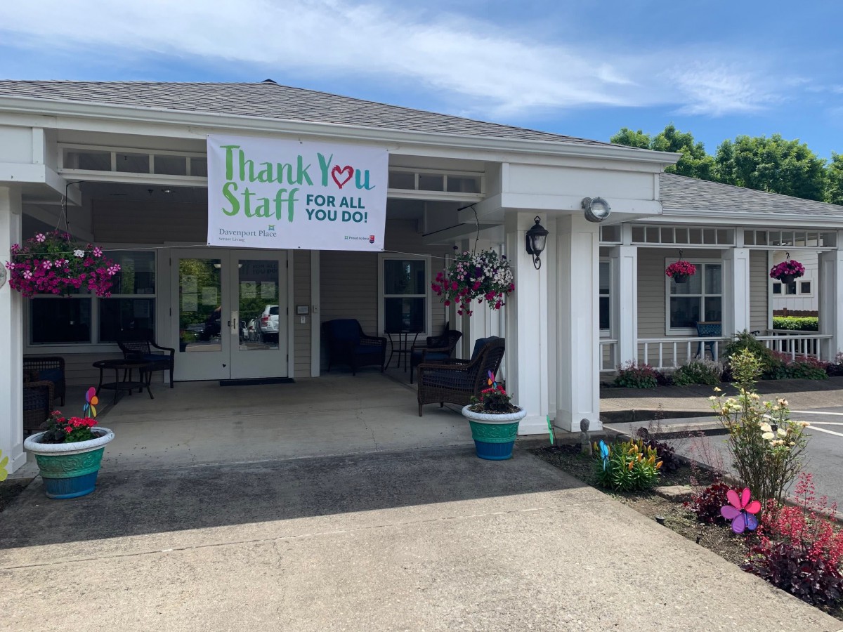 A building entrance with a 'Thank You Staff' banner and colorful flowers.