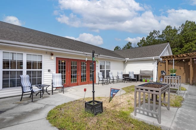 A cozy outdoor patio area with seating and tables in front of a building under a partly cloudy sky.