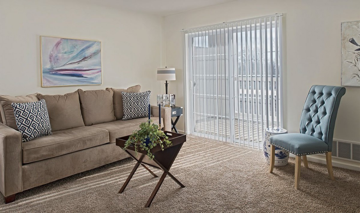 A cozy living room with a sofa, coffee table, and window blinds letting in natural light.