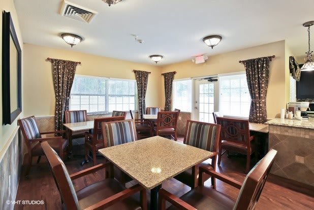 A cozy dining area with multiple tables and chairs, surrounded by large windows and curtains.