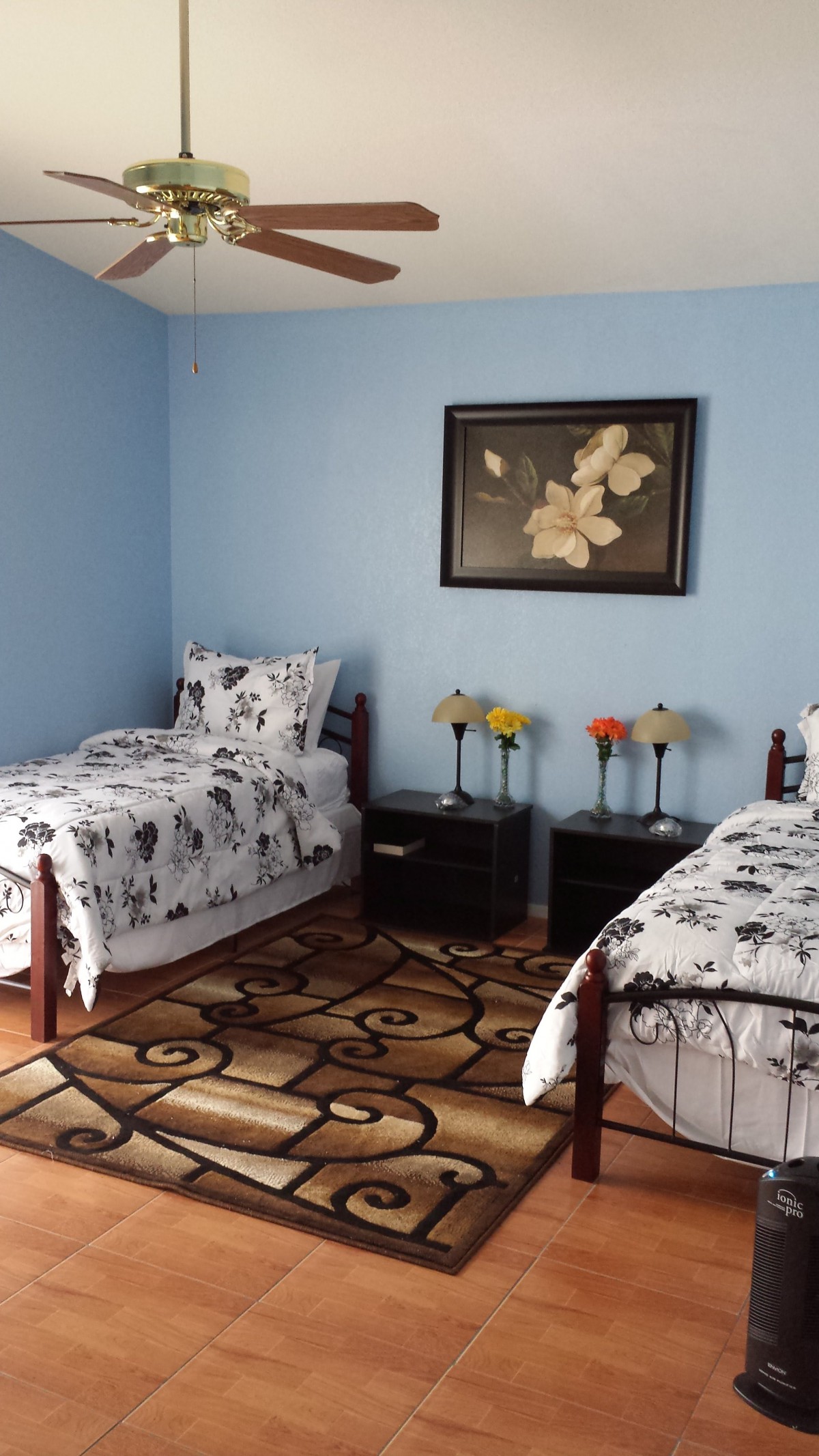 A cozy bedroom with two single beds, featuring floral bedding and a matching painting on blue walls.