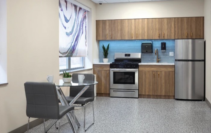 A modern kitchen with stainless steel appliances, wooden cabinets, and a small dining area.
