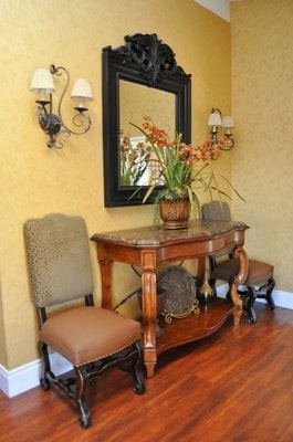 A well-decorated hallway featuring a wooden console table with chairs, a mirror, and ornamental wall sconces.