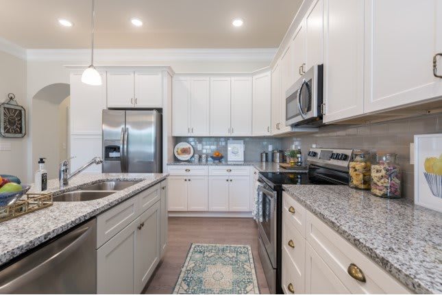 A modern kitchen with white cabinets, stainless steel appliances, and a granite countertop.