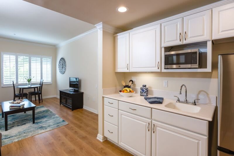 A modern apartment with a small kitchen and adjacent living area featuring white cabinets and wood flooring.