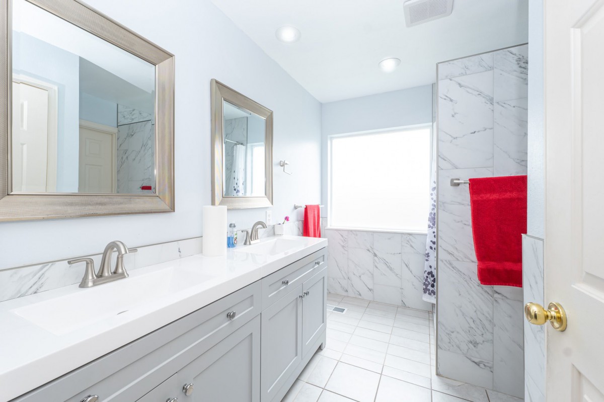 A modern bathroom with white tiles, featuring a sink, mirror, and red towels.