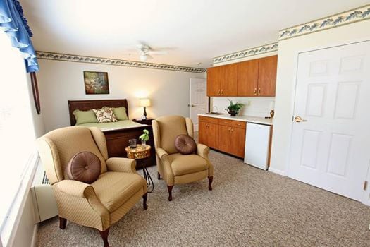 A cozy living space with armchairs, a bed, and a small kitchenette area.