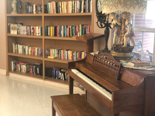 A cozy corner featuring a wooden piano and a bookshelf filled with various books.