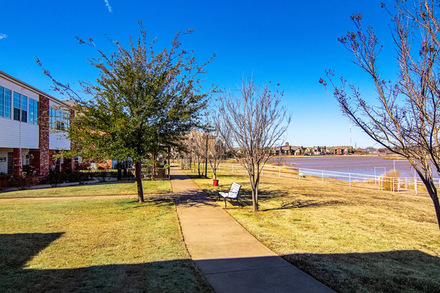 A scenic view of a park with a pathway leading to benches by the lake under a clear blue sky.