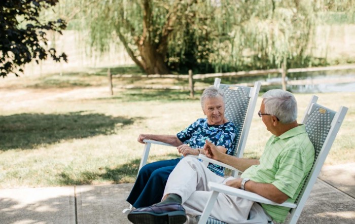 An elderly couple enjoying a conversation while seated in chairs outdoors.