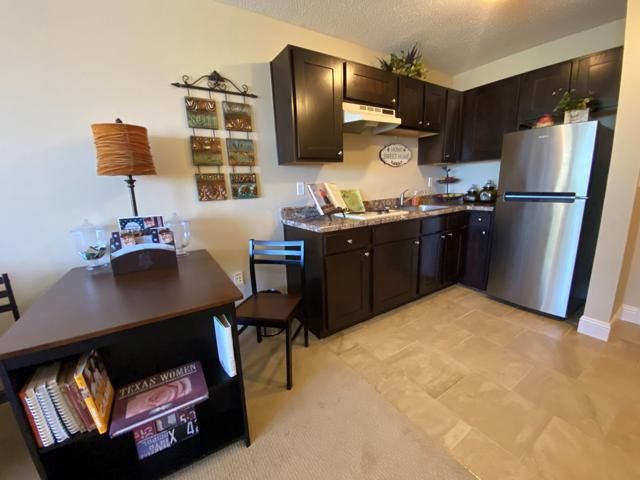 A cozy apartment kitchen with dark cabinets, a small dining area, and modern appliances.