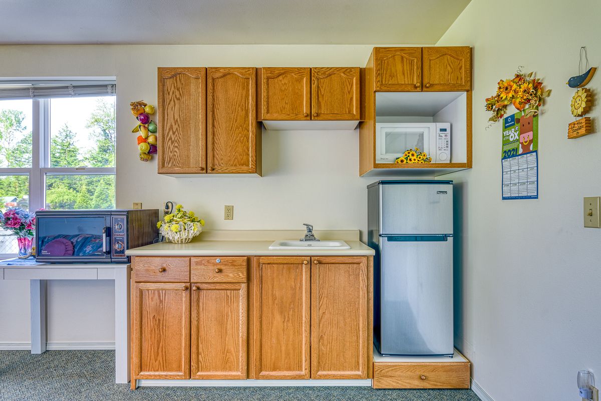 A compact kitchen with wood cabinetry, featuring a microwave, refrigerator, and sink.