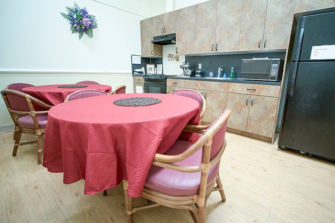 A kitchen and dining area with a round table covered in a red tablecloth, surrounded by chairs and wooden cabinetry in the background.
