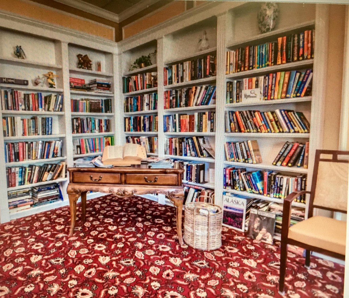 A cozy library with bookshelves filled with numerous books, a wooden table, and a patterned carpet.