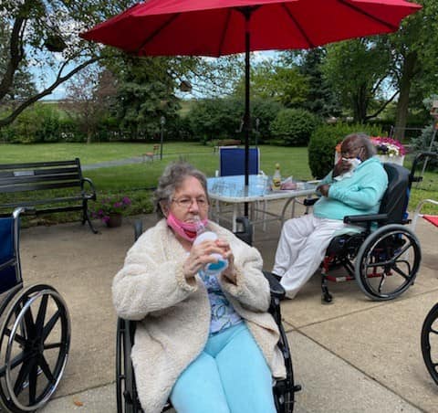 Seniors enjoying a sunny day at the park, sipping refreshments under a bright umbrella.