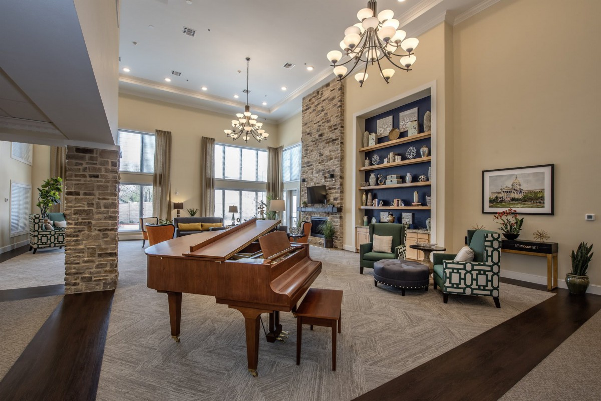 Luxurious living room with a grand piano, cozy seating area, chandelier lighting, and elegant fireplace.