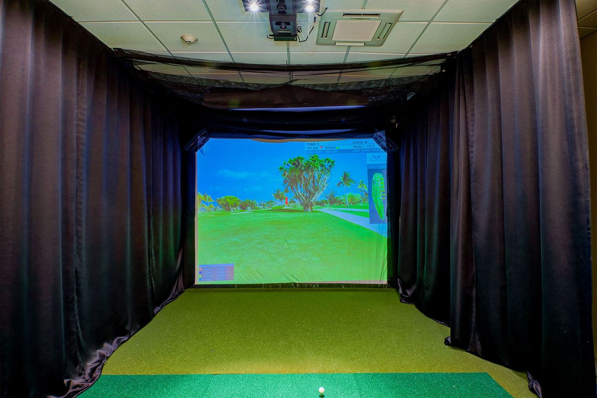 An indoor golf simulator setup with a virtual course displayed on the screen.
