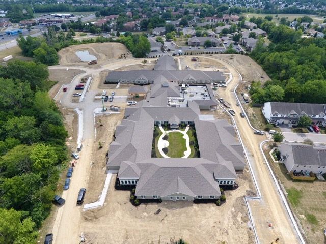 Aerial view of a construction site featuring a large building and surrounding land development in a suburban area.