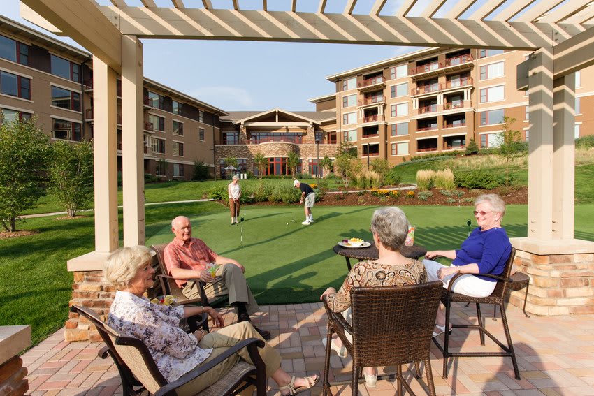 Seniors enjoy a sunny day outdoors, socializing and playing lawn games in a retirement community.