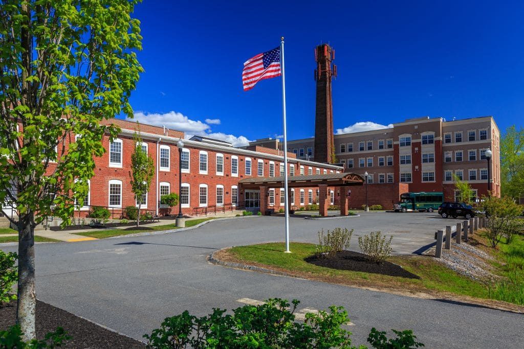 A large brick building with an American flag in the foreground under a clear blue sky.